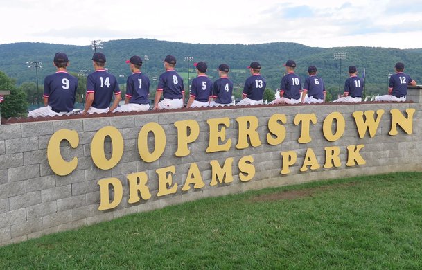 Youth baseball team sitting on the Cooperstown Dreams Park sign